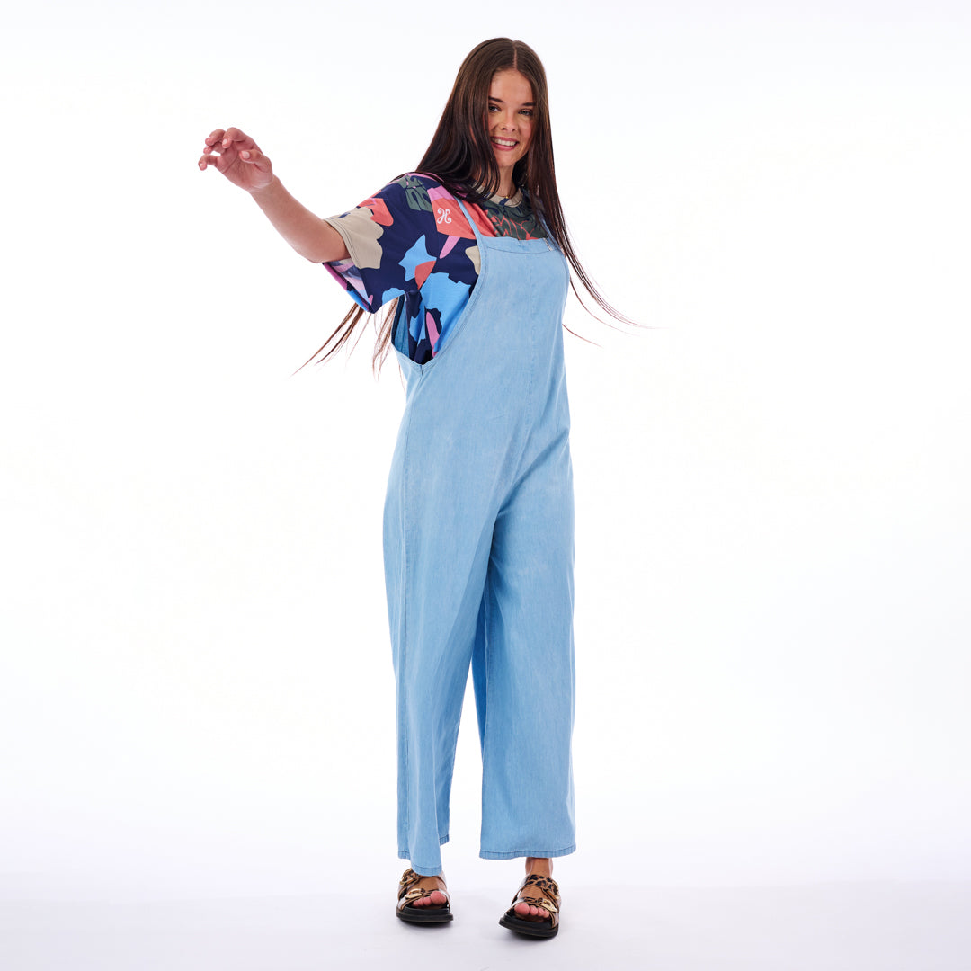 Woman wearing a colorful top and light blue jumpsuit on a white background