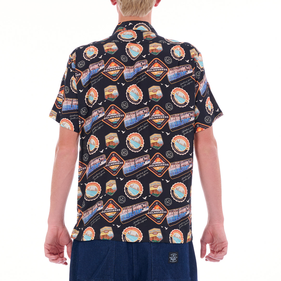 Person wearing a patterned shirt with scenic designs on a white background