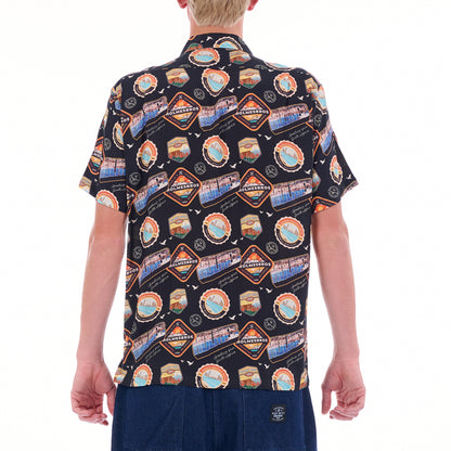 Person wearing a patterned shirt with scenic designs on a white background