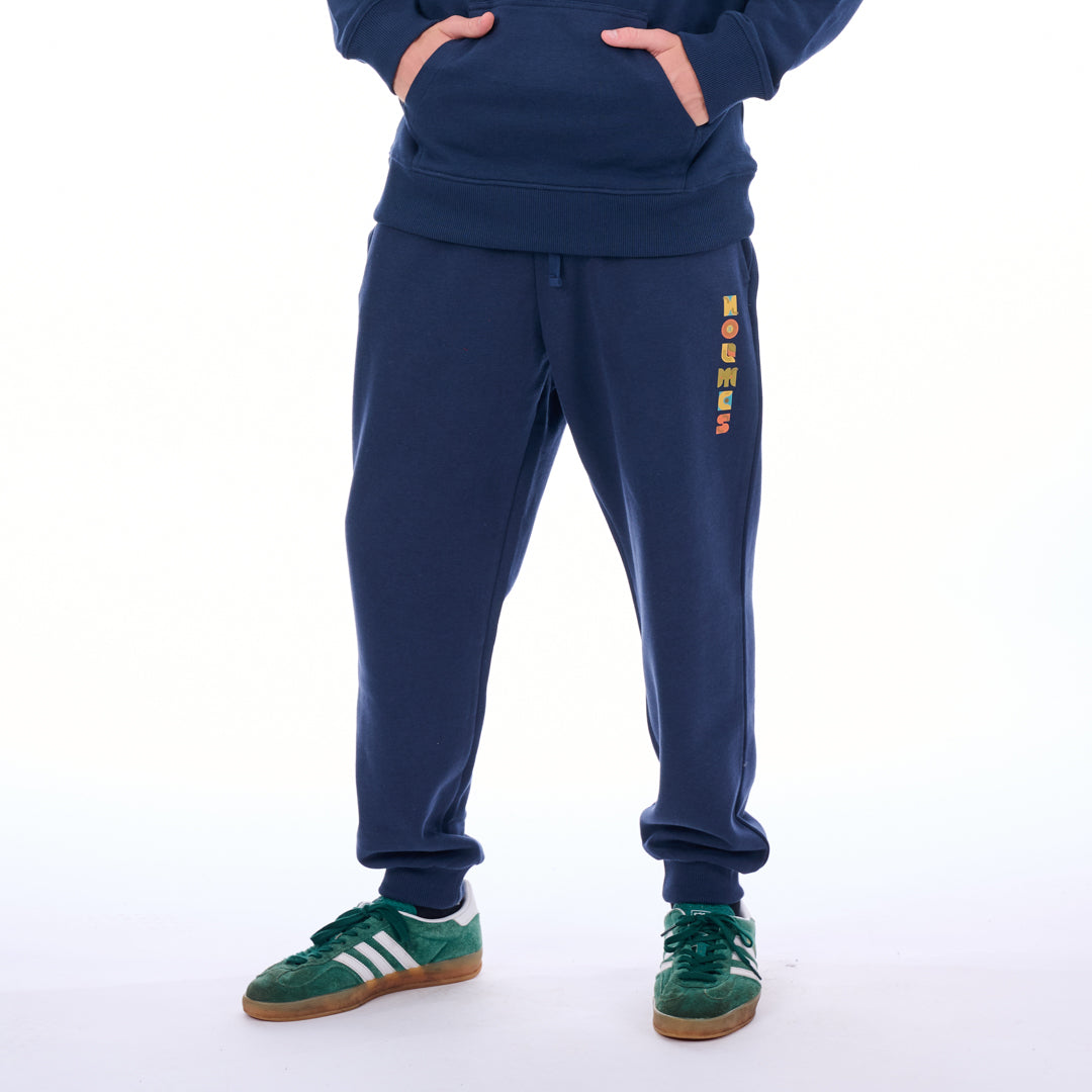 Person wearing a navy tracksuit with colorful text on the pants against a white background