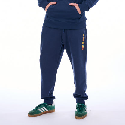 Person wearing a navy tracksuit with colorful text on the pants against a white background