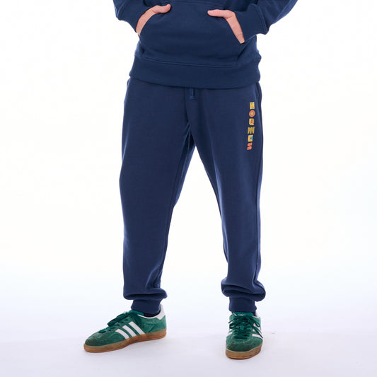 Person wearing a navy tracksuit with colorful text on the pants against a white background