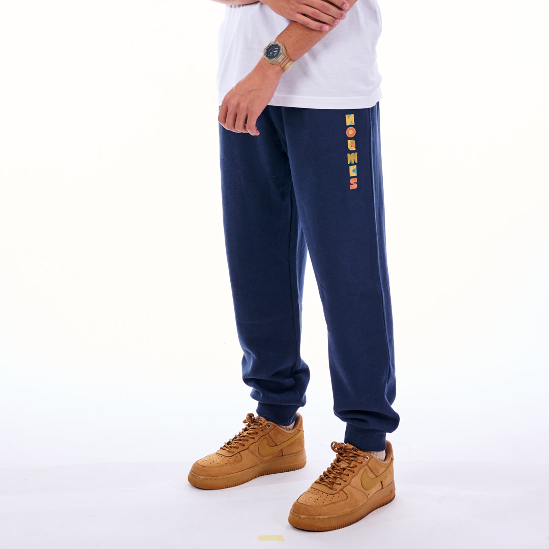 Person wearing navy sweatpants with colorful text design and tan shoes on a white background