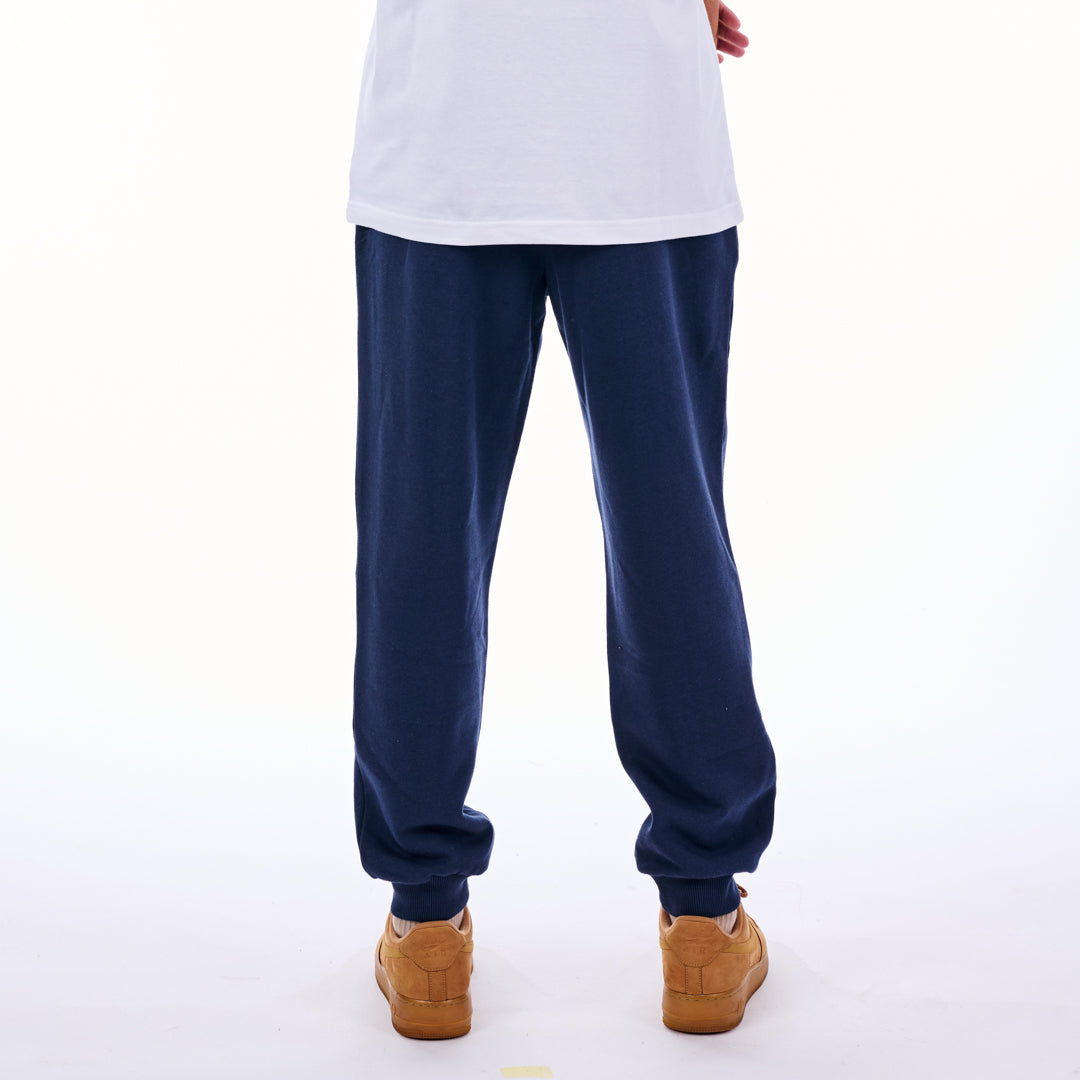 Person wearing navy blue sweatpants and brown shoes on a white background