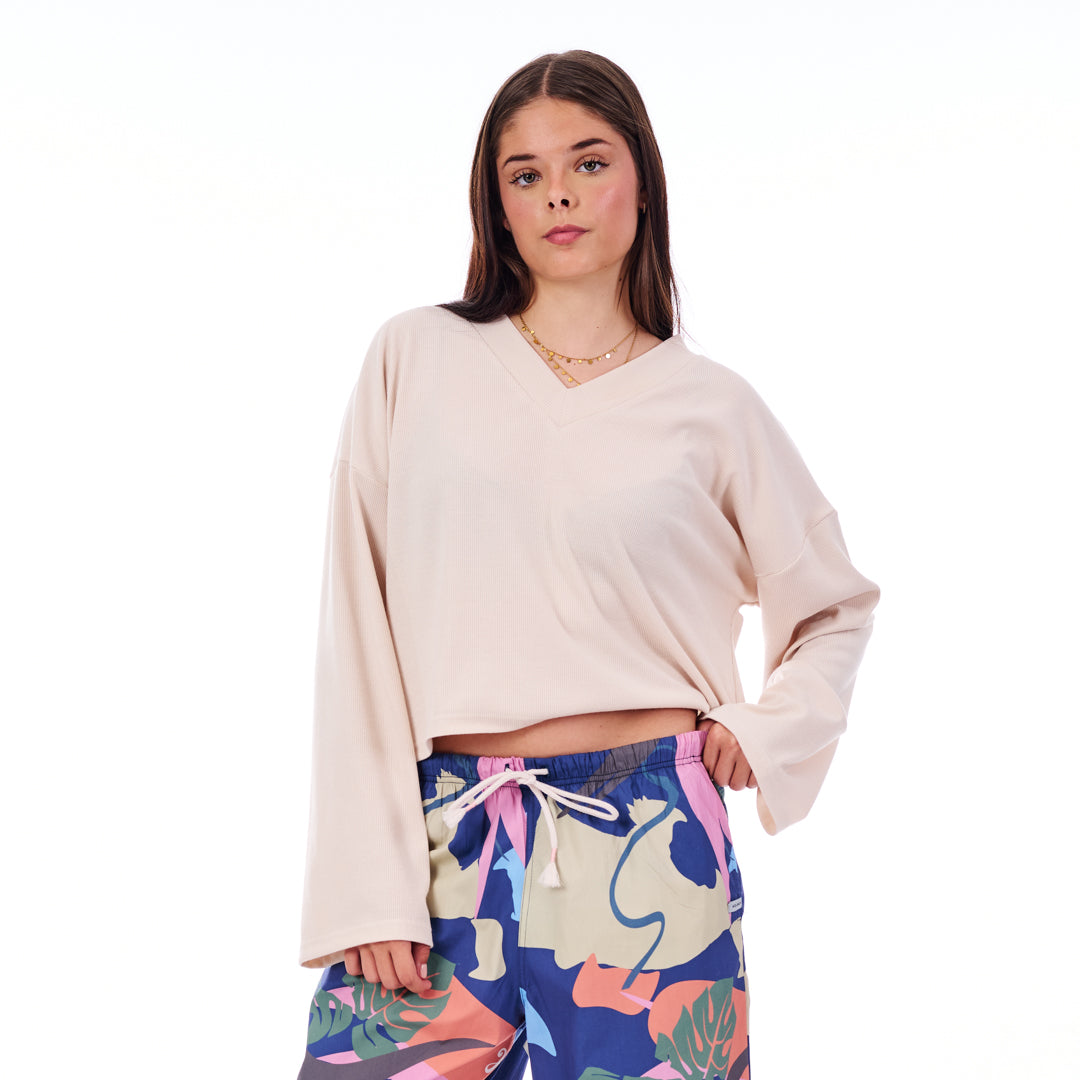 Woman wearing a beige long-sleeve top and colorful floral pants on a white background