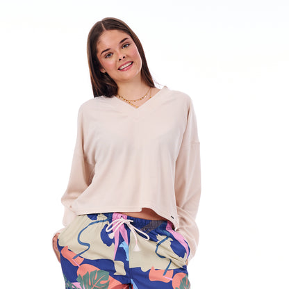 Woman wearing a beige long-sleeve top and colorful patterned pants on a white background