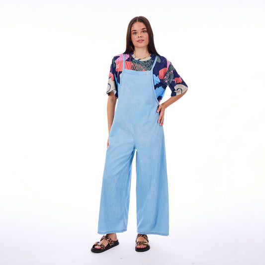 Woman wearing a colorful top and light blue overalls on a white background