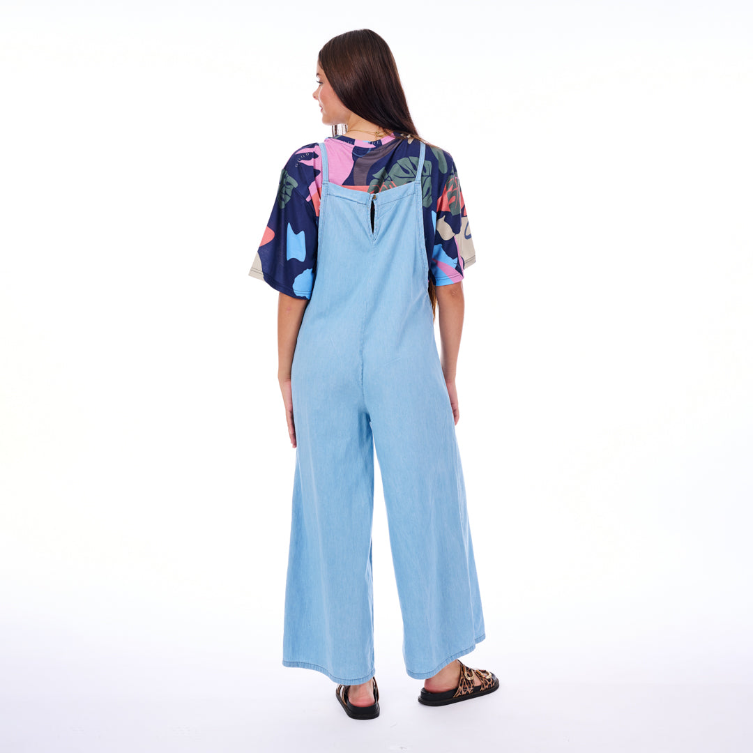 Woman wearing a light blue jumpsuit with a colorful top on a white background
