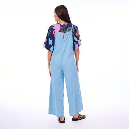 Woman wearing a light blue jumpsuit with a colorful top on a white background