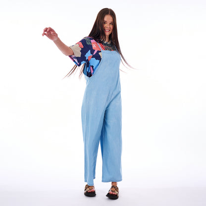 Woman wearing a colorful top and light blue jumpsuit on a white background